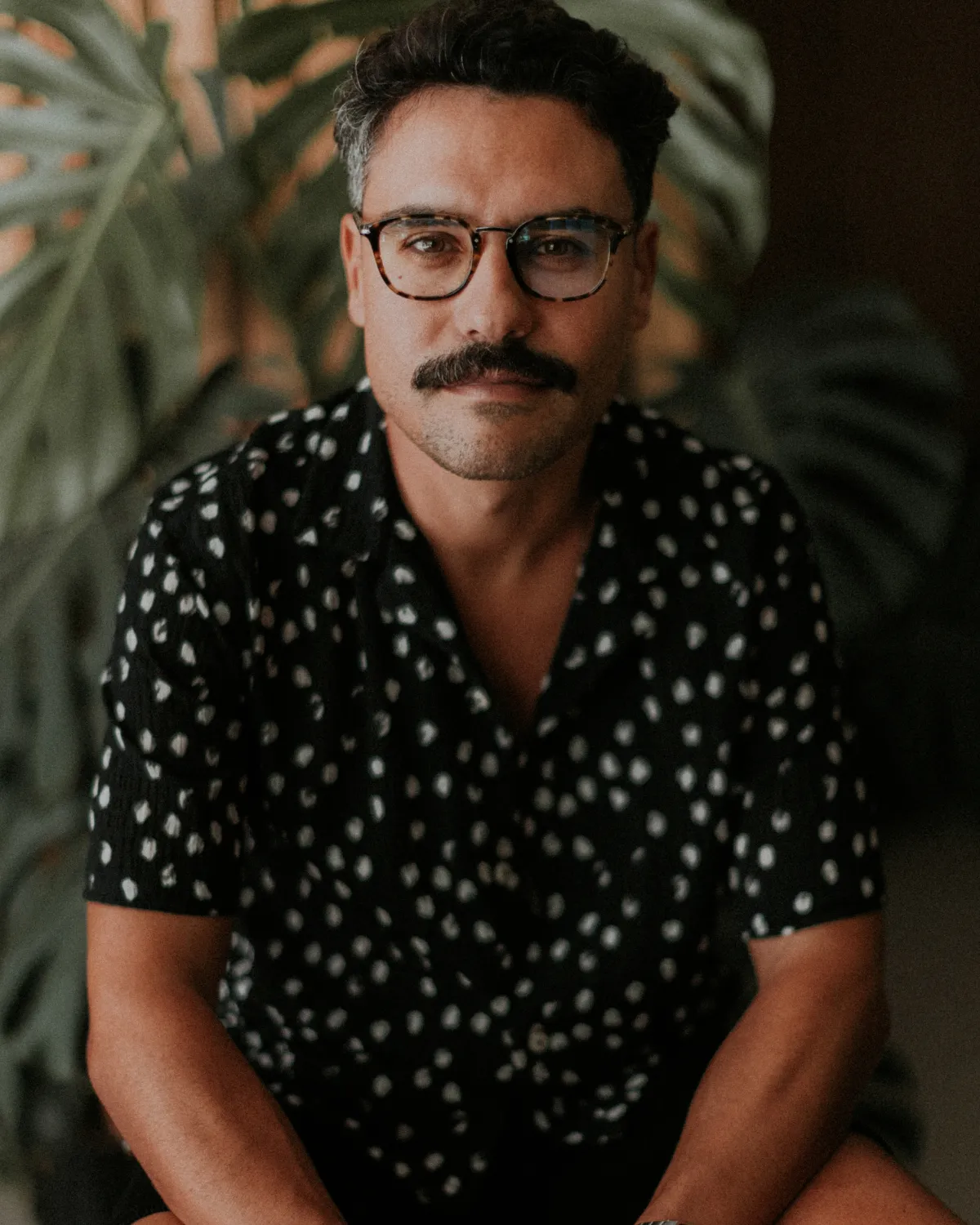 Retrato de Pedro Rodrigues, escritor, tradutor e ilustrador português, sentado em frente a um fundo de plantas verdes.